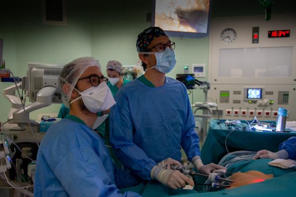 2 doctors perform an operation while other members of the surgical team are seen around them